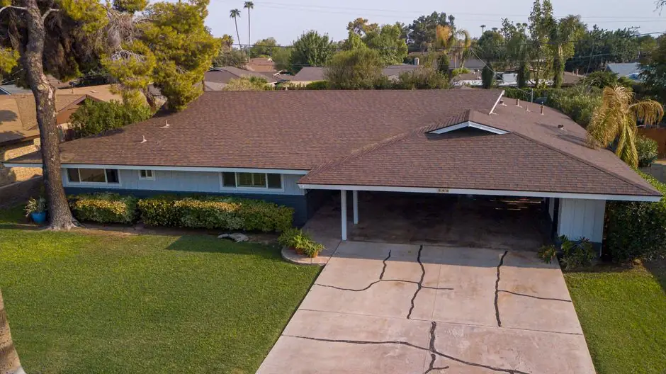 Aerial view of a suburban house with a brown roof surrounded by greenery.